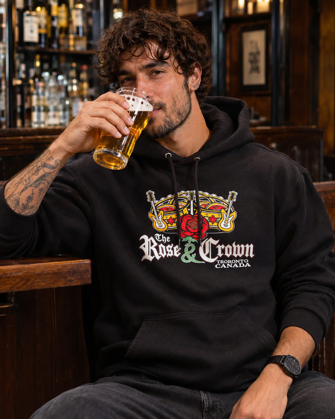 Model enjoying a pint at the pub wearing the black Rose & Crown hoodie